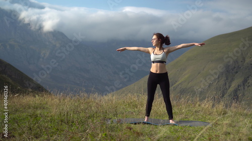 Young woman in tracksuit is engaged in yoga performing triconasana pose in the mountains. The camera moves to create a parallax effect.