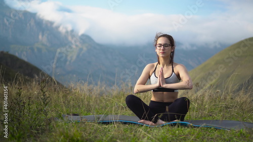A young woman in a tracksuit practices yoga in the mountains. The camera moves to create a parallax effect.