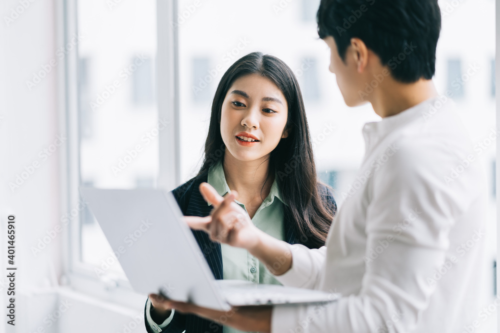 Two Asian colleagues are discussing the work. The businessman is holding a laptop in his hand Two Asian colleagues are discussing the work. The businessman is holding a laptop in his hand