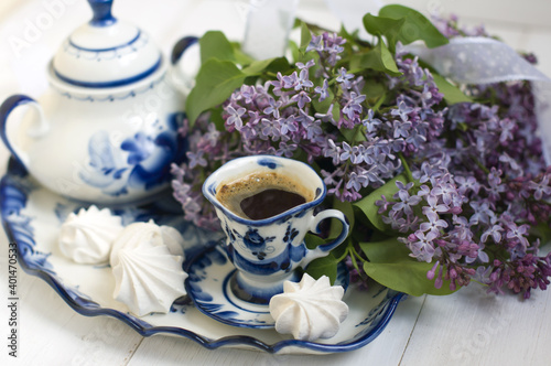lilac flowers, sugar bowl, cup of coffee, meringues on a tray on a light background