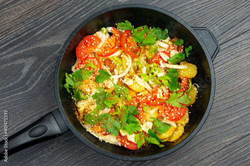 cooked fried potatoes with herbs, spices and vegetables in a black pan on a wooden table