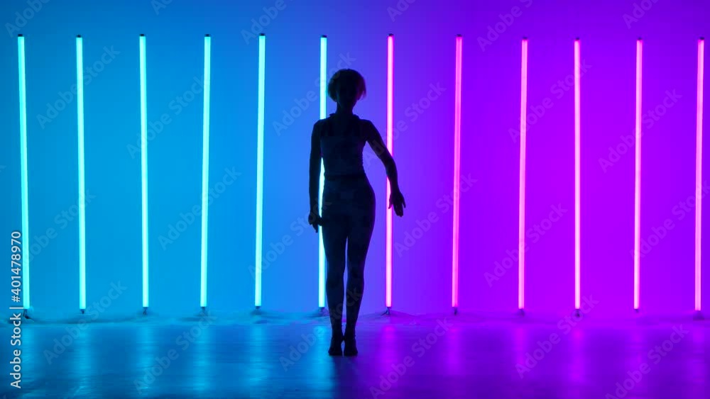 Silhouette of a graceful young woman in full growth dancing elements of modern dance in the studio on a blue purple background with neon lighting. Street dance. Dance poster design. Silhouette of a graceful young woman in full growth dancing elements of modern dance in the studio on a blue purple background with neon lighting. Street dance. Dance poster design.