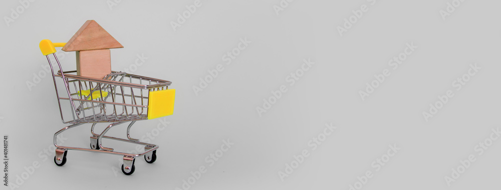 Banner of a model of a wooden makeshift house in a grocery cart with a yellow handle on a gray background. Horizontal format. Side view. Copyspace