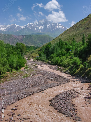 Peaceful countryside scenery with Academy of Sciences Pamir mountain range in background and red river Surkhob, Rasht valley, Tajikistan in foreground photo