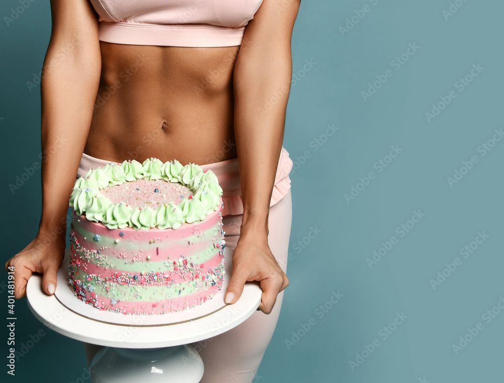Foto de Closeup on big heavy birthday holiday cake with cream fitness woman  in top bra and pants holds is carrying in hands over blue background with  copy space. Figure, present, birthday