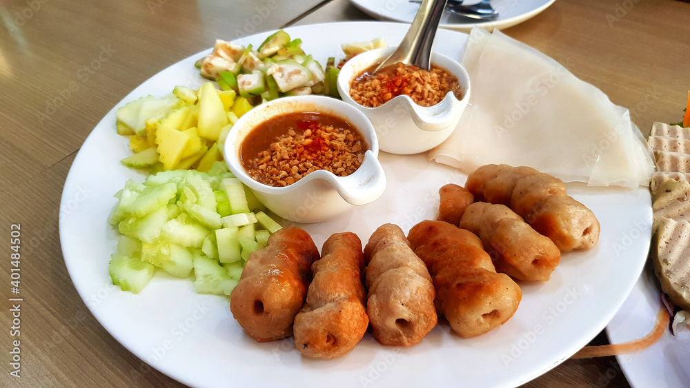 Vietnamese meatball wrap with fresh sliced of cucumber, sour mango, garlic, raw banana and sweet peanut bean sauce on white dish or table. This food call Namnueng. Famous in Vietnam. Vietnamese meatball wrap with fresh sliced of cucumber, sour mango, garlic, raw banana and sweet peanut bean sauce on white dish or table. This food call Namnueng. Famous in Vietnam.
