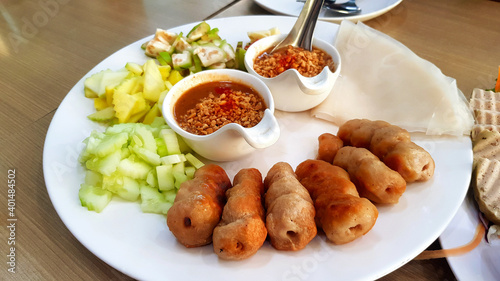Vietnamese meatball wrap with fresh sliced of cucumber, sour mango, garlic, raw banana and sweet peanut bean sauce on white dish or table. This food call Namnueng. Famous in Vietnam. 