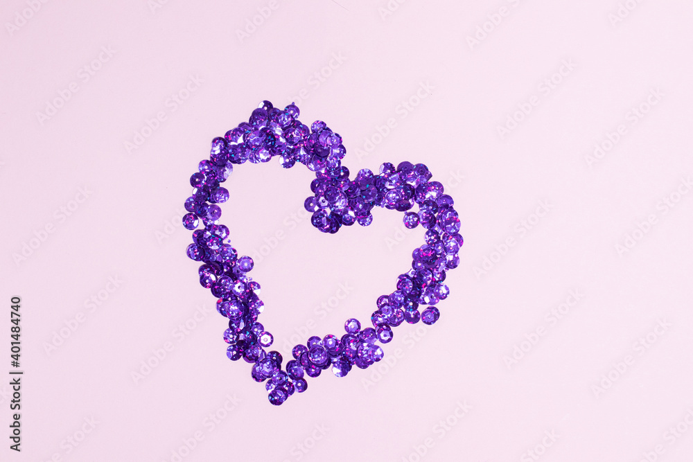 Purple sequins scattered in the form of heart on pink background. Valentine's Day decor