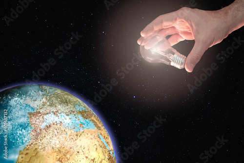 Hand holding a light bulb illuminating the planet earth. Concept of energy photo