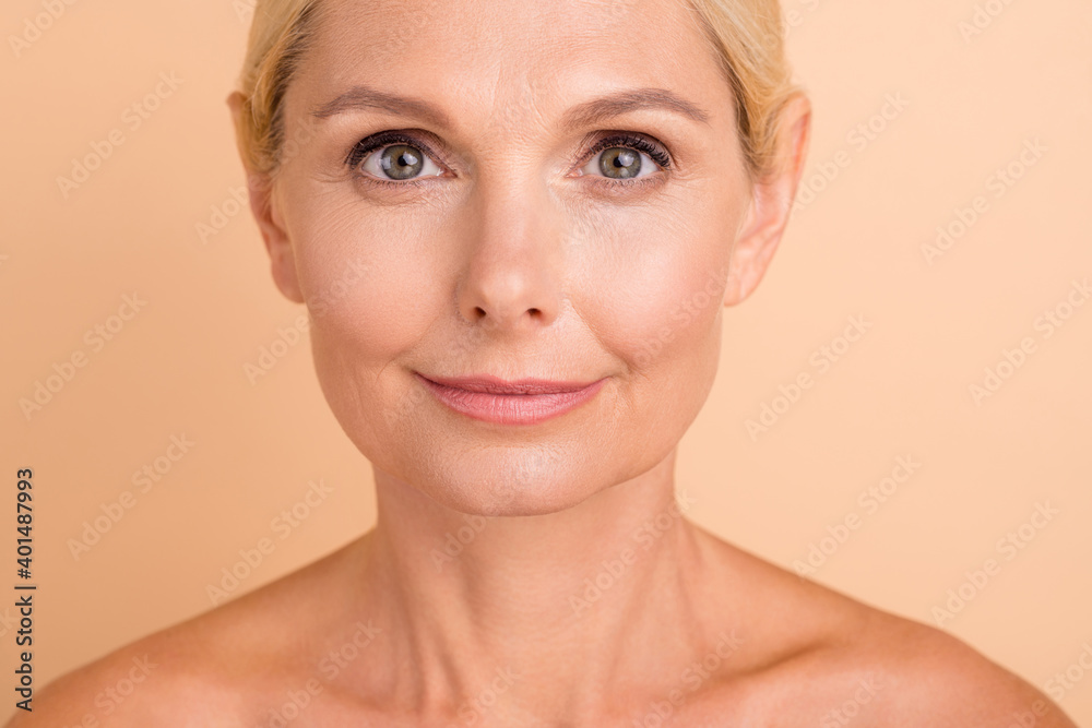 Cropped close-up portrait of nice-looking middle aged lady with smooth skin isolated over beige pastel color background Cropped close-up portrait of nice-looking middle aged lady with smooth skin isolated over beige pastel color background