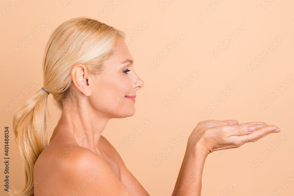 Profile photo of beauty aged lady naked shoulders perfect facial skin hold open palms isolated beige color background Profile photo of beauty aged lady naked shoulders perfect facial skin hold open palms isolated beige color background