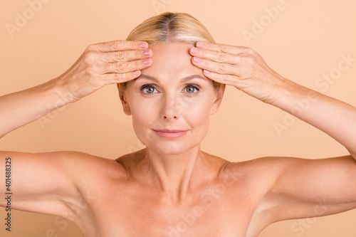 Photo of natural beauty aged lady naked shoulders touch forehead perfect skin look mirror anti age cream uplift action tightening care isolated beige color background