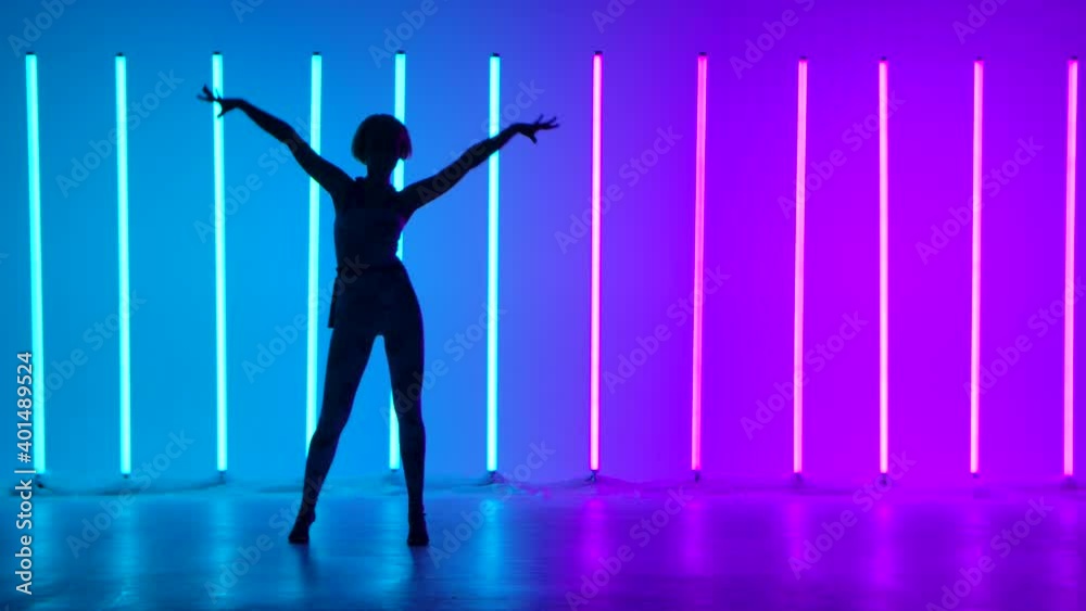 Silhouette of a graceful young woman in full growth dancing elements of modern dance in the studio on a blue purple background with neon lighting. Street dance. Dance poster design. Slow motion. Silhouette of a graceful young woman in full growth dancing elements of modern dance in the studio on a blue purple background with neon lighting. Street dance. Dance poster design. Slow motion.
