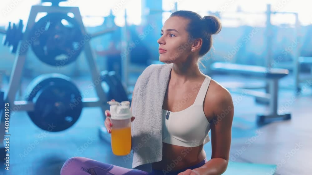 Caucasian beautiful sweaty woman after workout drinking protein juice shake in bottle smiling cheerfully to camera. Sportswoman. Active and healthy lifestyle.