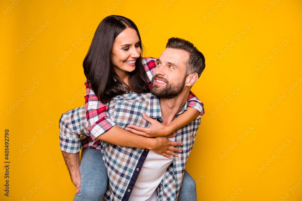 Photo portrait of woman riding man's back looking at each other isolated on vivid yellow colored background Photo portrait of woman riding man's back looking at each other isolated on vivid yellow colored background
