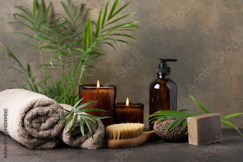 Spa composition with candles, towels, massage brush, volcanic pumice stone, care cream in dark glass bottle and green tropical plants. Beauty spa treatment and relax concept