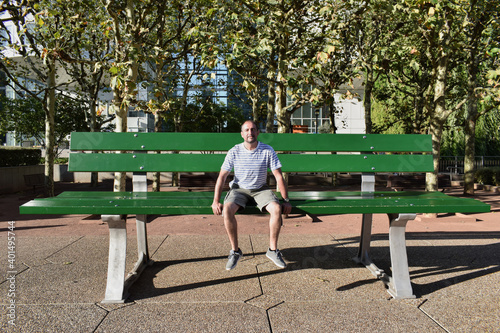 Hombre adulto sentado en un gran banco verde dando la sensasion y perspectiva de ser enano y estar empequeñecido en los jardines de La Defense de Paris photo