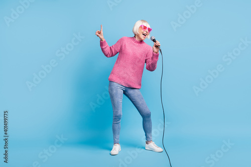 Photo portrait full body view of elderly lady singing pointing finger up holding mic in one hand isolated on pastel blue colored background photo
