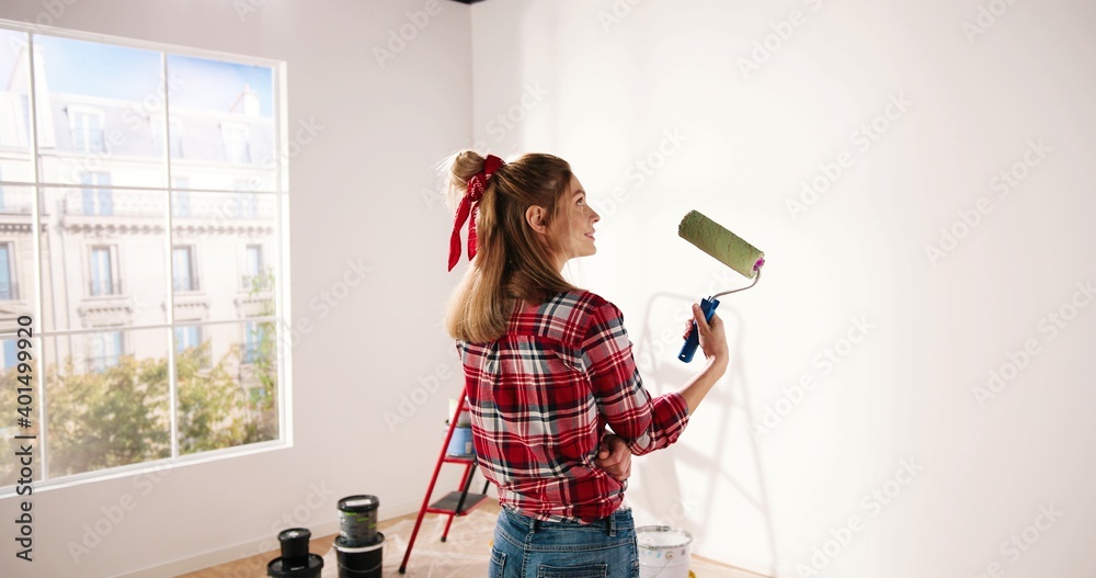 Close up. Side view of pretty joyful Caucasian woman alone painting room in new house in green color. Beautiful female renovating home painting wall using roller brush redesigning apartment - obrazy, fototapety, plakaty 