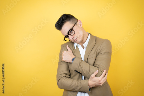 Young business man over isolated yellow background hugging oneself happy and positive, smiling confident