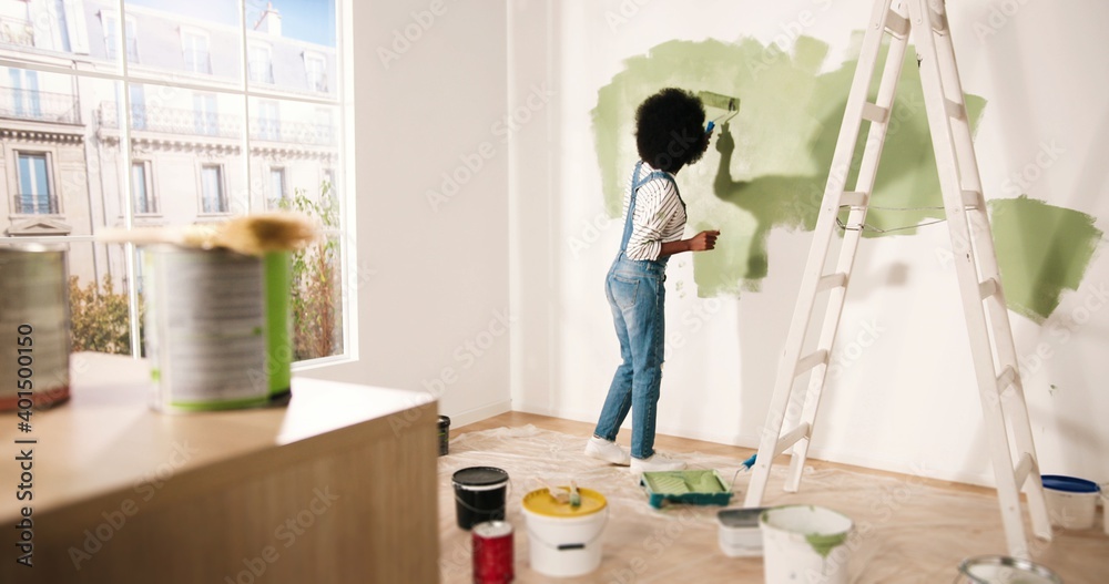 Εκτύπωση καμβά Young African American female alone painting wall with roller brush in olive color while renovating apartment