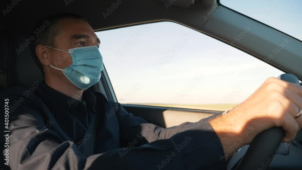 A man driver sits in a car with a protective mask during the coronavirus pandemic. A businessman in a medical mask is driving a car. Traveling by car during a pandemic with protective equipment A man driver sits in a car with a protective mask during the coronavirus pandemic. A businessman in a medical mask is driving a car. Traveling by car during a pandemic with protective equipment