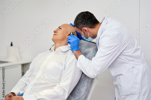 Doctor ENT checking ear with otoscope to man patient at hospital