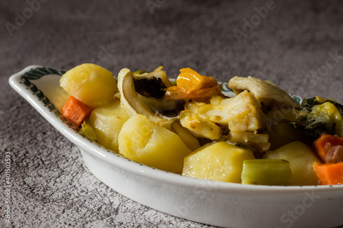 Stewed cod with potatoes, celery, carrots and yellow cherry tomatoes on a gray background. Selective focus.