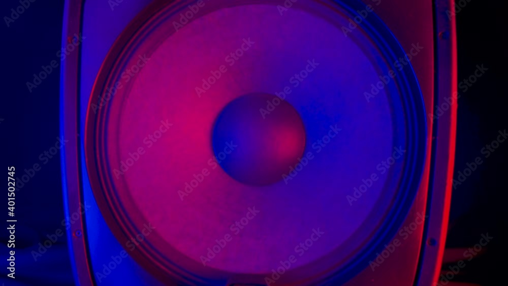 Playing speaker membranes lit by colourful disco neon lights. Powerful, modern loudspeakers vibrate bouncing to the rhythm electronic music. Close up. Slow motion.