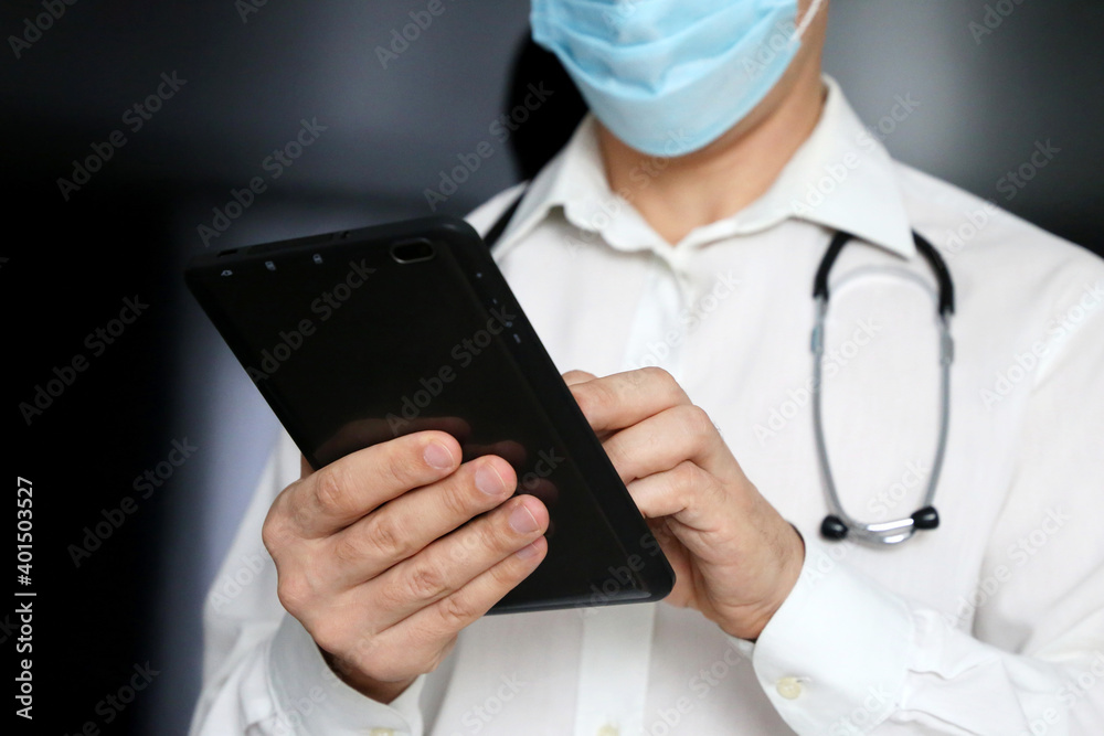 Man doctor in a medical mask with a tablet PC in hands. Work of medical staff during the covid-19 coronavirus epidemic Man doctor in a medical mask with a tablet PC in hands. Work of medical staff during the covid-19 coronavirus epidemic