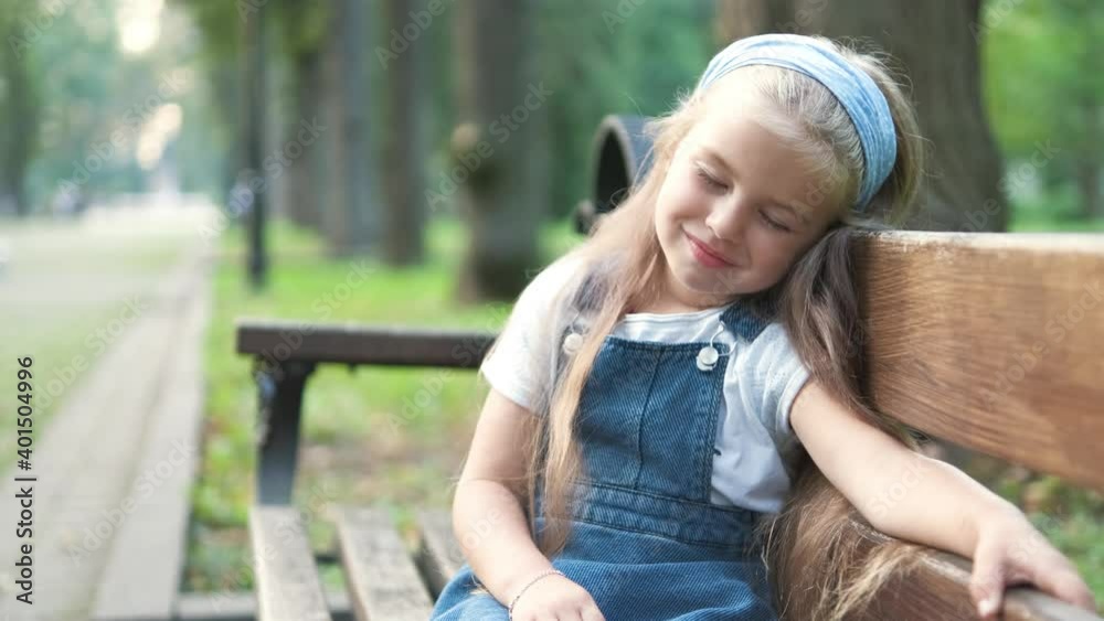 Small tired child girl sitting on a bench with closed eyes resting in summer park. Small tired child girl sitting on a bench with closed eyes resting in summer park.