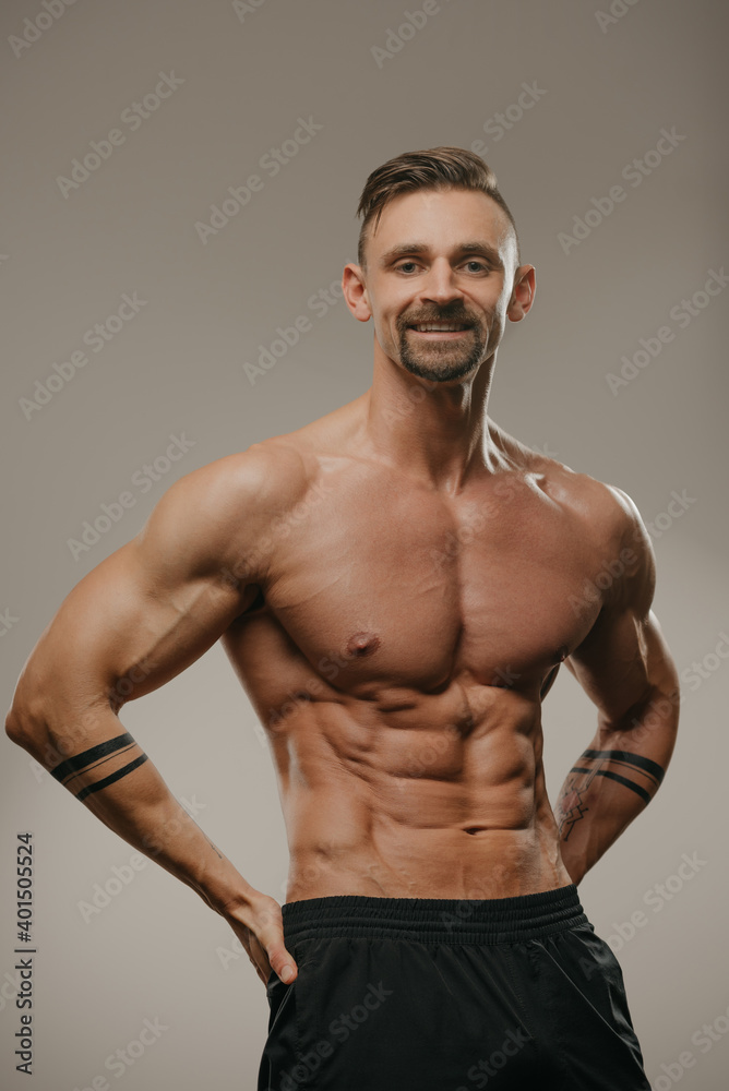 A smiling muscular man with a beard is posing. The athletic guy is squeezing his muscles. A bodybuilder with tattoos on his forearms is standing with his hands on his hips A smiling muscular man with a beard is posing. The athletic guy is squeezing his muscles. A bodybuilder with tattoos on his forearms is standing with his hands on his hips