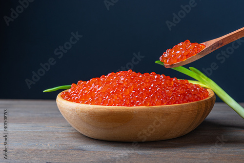 Red caviar in a wooden cup on a wooden background with a spoon.