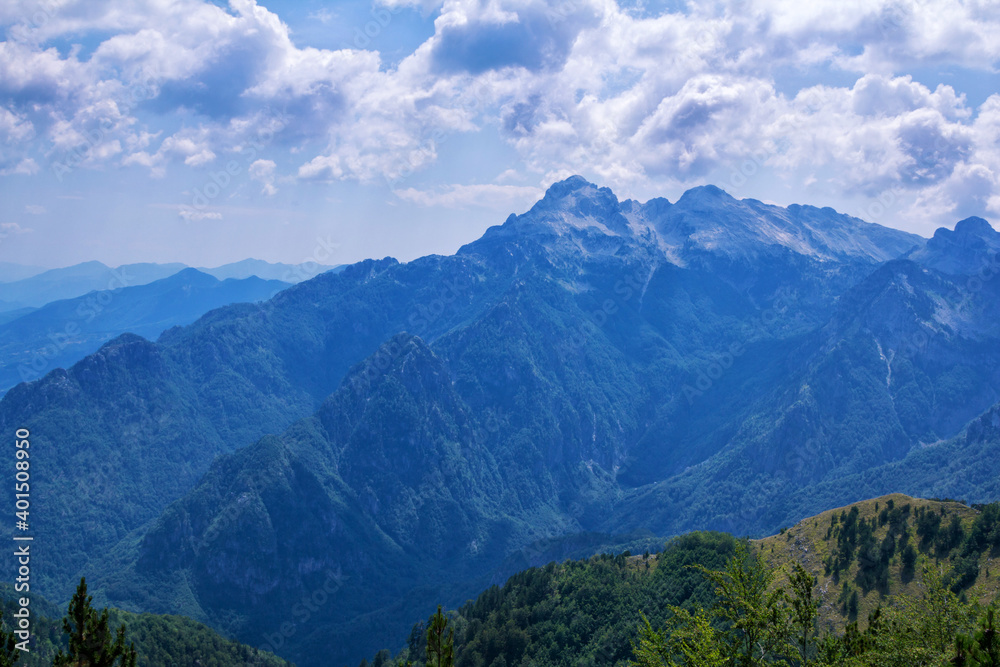 Summer landscape – beautiful Albanian mountains, covered with green trees and clouds on blue sky.