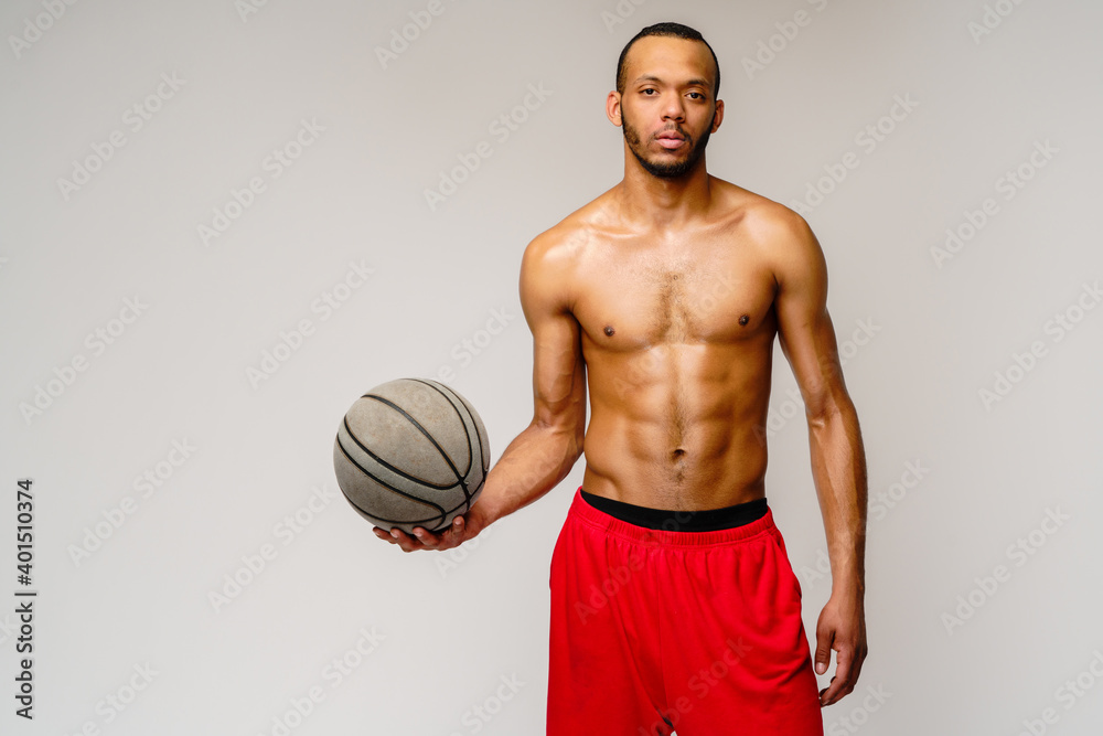 Muscular african american sportsman playing basketball shitless over light grey background