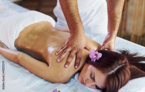 Purple flower lying down. Man does massage to the young woman in white towel indoors