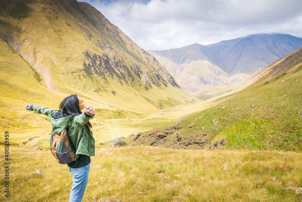 Female backpacker stands on the rock and enjoys stunning mountain views in Juta valley. KAzbegi national park exploration