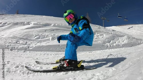 Freestyle skiing. Little boy jumping in a snowpark.  
A 6 year old child enjoys a winter holiday in the Alpine resort. Stabilized footage. Slow motion. 