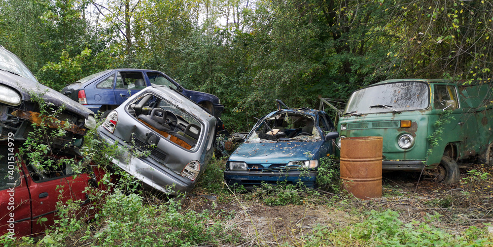 A few old damaged rusty cars,broken,piled up,with rusty barrel,green nature as backdrop.Disposal of abandoned cars A few old damaged rusty cars,broken,piled up,with rusty barrel,green nature as backdrop.Disposal of abandoned cars