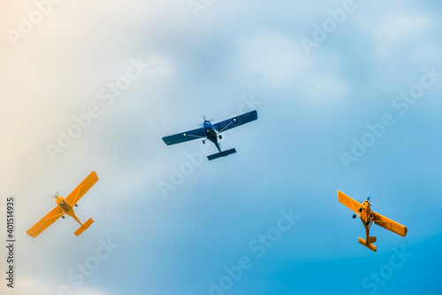 three small two-pilot airplanes boldly making turns in the blue cloudy sky 