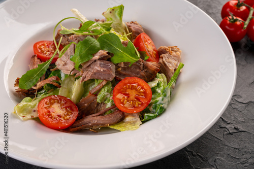 salad with meat and cherry tomatoes in a white plate on a dark background