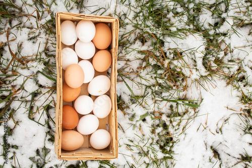 A wicker basket of collected chicken eggs lies on the grass in the snow