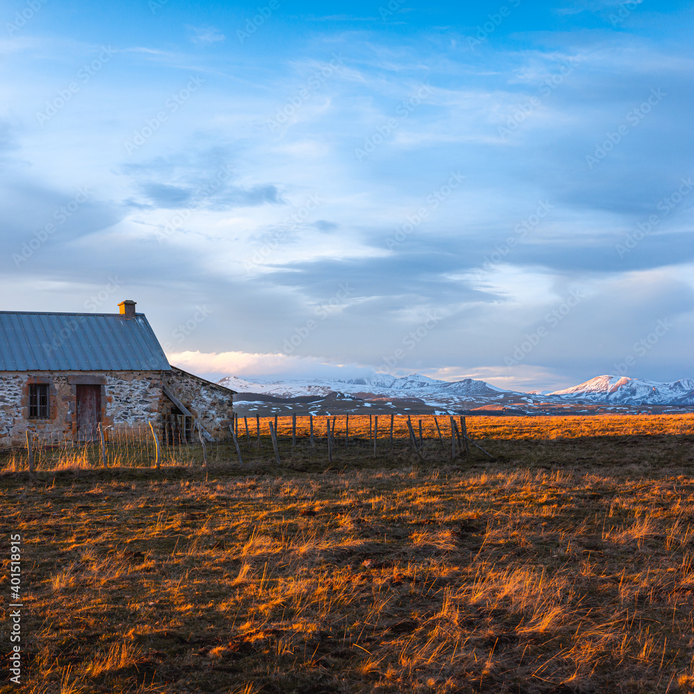 Old barn in field and snow caped mountains at sunset