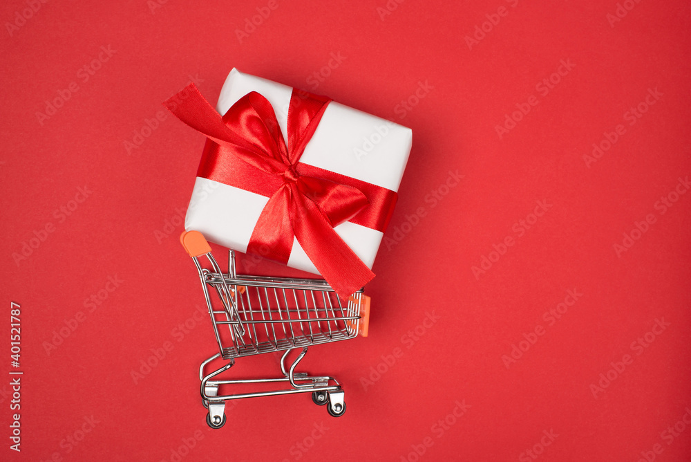 Top above flatlay close up profile view photo of metal silver trolley basket on wheels carrying big present box isolated red bright color background