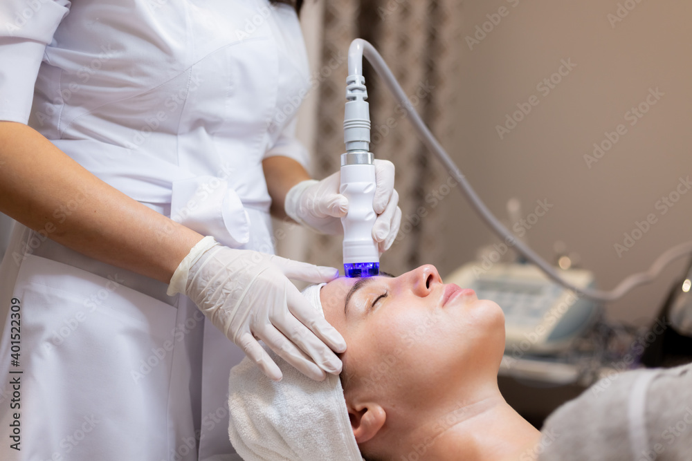 A young beautiful girl lies on the beautician's table and receives procedures with a professional apparatus for skin rejuvenation and moisturizing A young beautiful girl lies on the beautician's table and receives procedures with a professional apparatus for skin rejuvenation and moisturizing