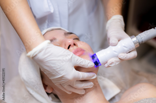 A young beautiful girl lies on the beautician's table and receives procedures with a professional apparatus for skin rejuvenation and moisturizing