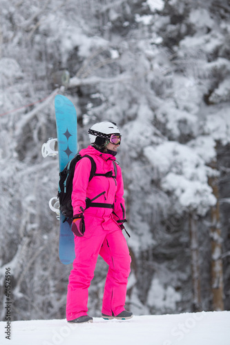 Woman in bright pink sportive overall with snowboard on the backpack having fun outisde in snowy day. Winter restorative escape concept. Vertical orientation