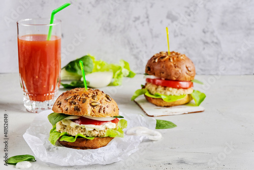 Vegetarian hamburger with tomato, lettuce, onion, bean cutlet and grain bun is an alternative to the usual hamburger. Next to a glass of fresh tomato juice. The concept of healthy eating.