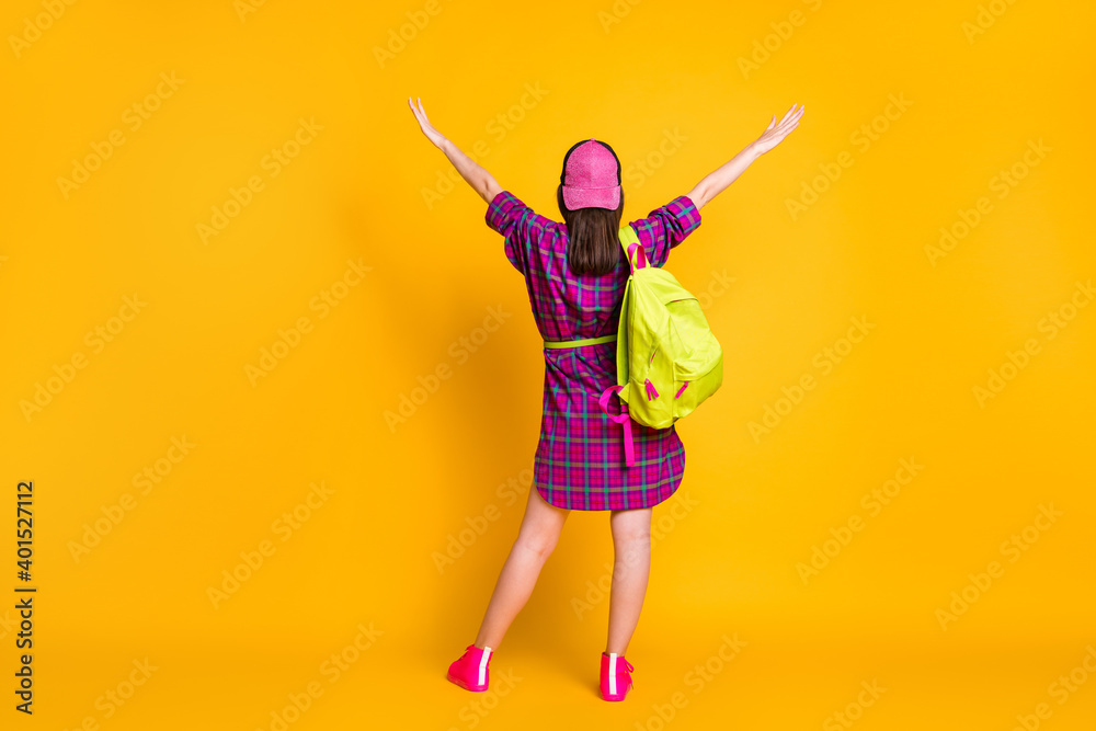 Full length rear back view photo of girl raising hands wear pink dress sneakers bag headwear isolated yellow color background Full length rear back view photo of girl raising hands wear pink dress sneakers bag headwear isolated yellow color background