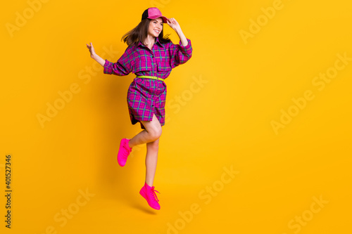 Full size portrait of pretty person jumping looking empty space purple headwear isolated on yellow color background